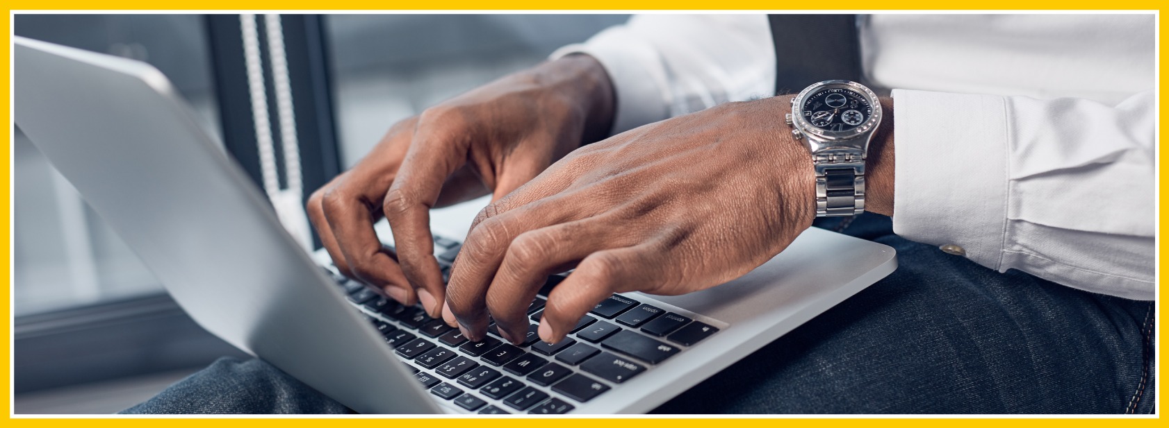 Zoomed in on a gentleman typing away on his laptop as he sits away from his desk.