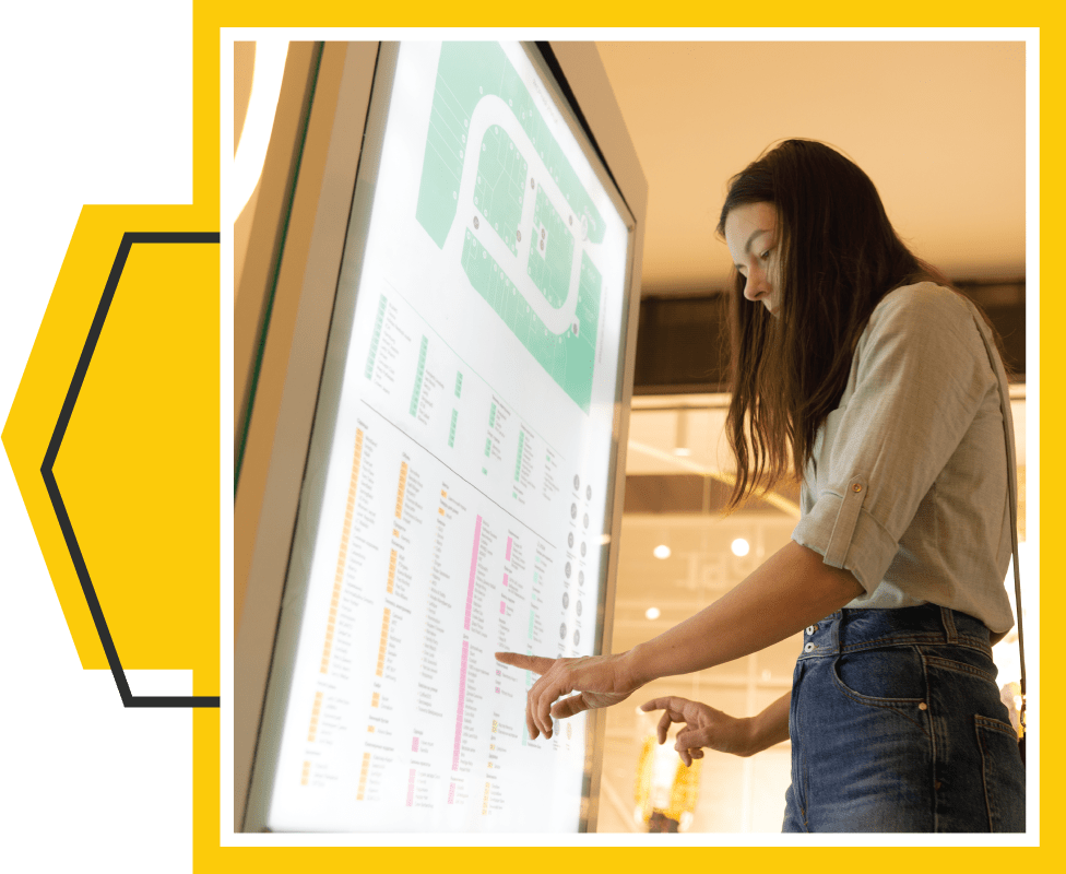 Framed image of a woman utilizing a navigational digital sign in a large shopping mall