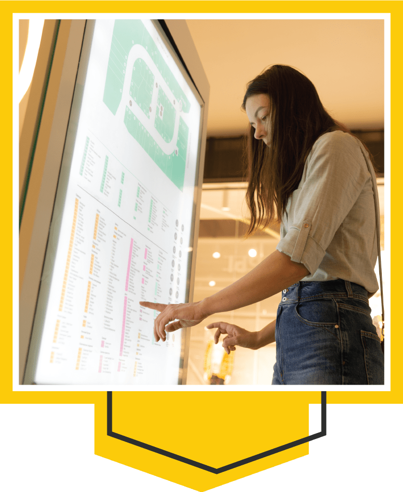 Framed image of a woman utilizing a navigational digital sign in a large shopping mall