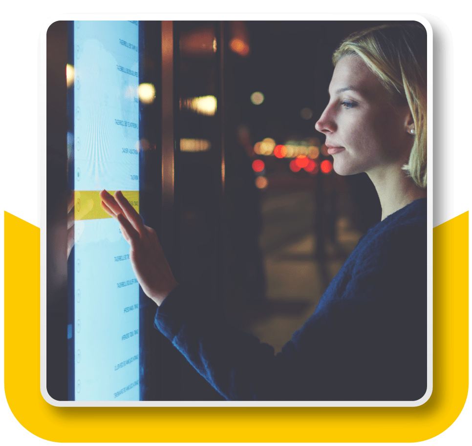 Framed image of a woman interacting with a large touchscreen kiosk. She is scrolling through a list of options.