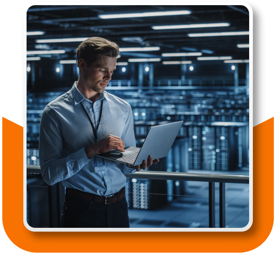 Framed Image: A man is standing in the foreground working on a laptop. In the background are rows and rows of data servers.