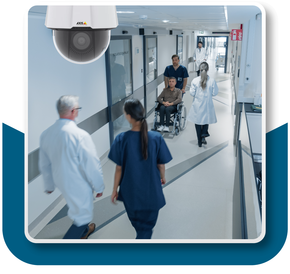 Framed Image: Surveillance camera trained down a hallway in a hospital. Various doctors, nurses, and a patient or two are occupying the hallway.