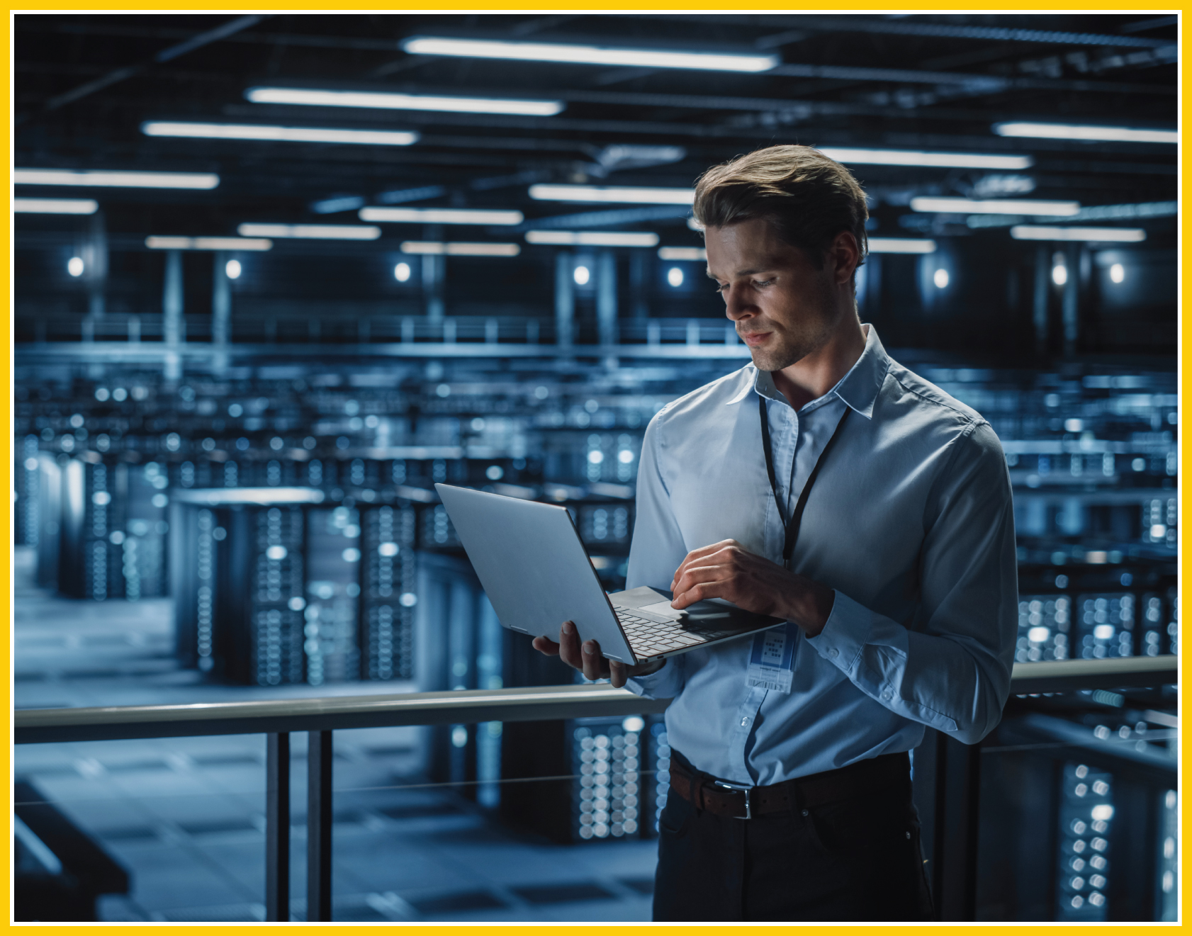 Employee in the foreground working on his laptop. Rows upon rows of servers are in the background of this data center. 